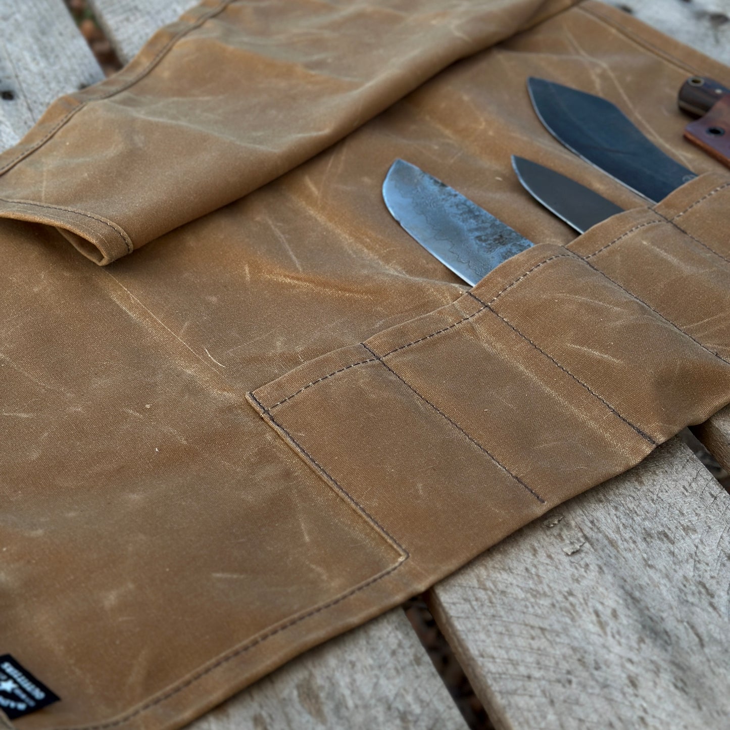 Close-up of a waxed canvas knife and tool roll featuring multiple knife pockets and durable leather straps.