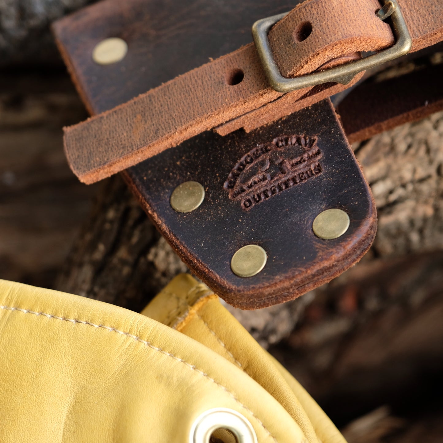 Close-up of a premium Crazy Horse leather axe mask strap with brass studs and logo on wood background.