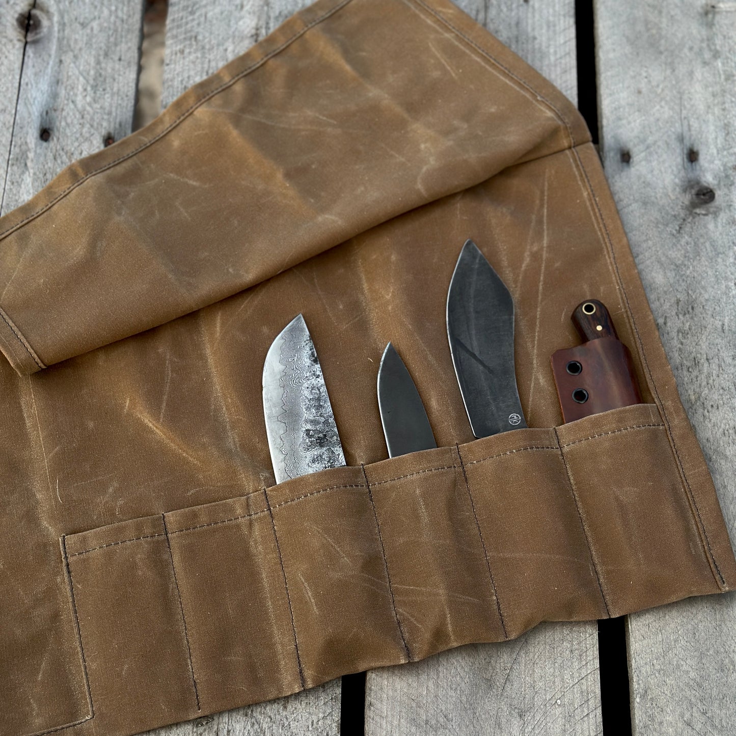 Waxed canvas knife roll with three knives and a tool, showcasing durable design and storage pockets.