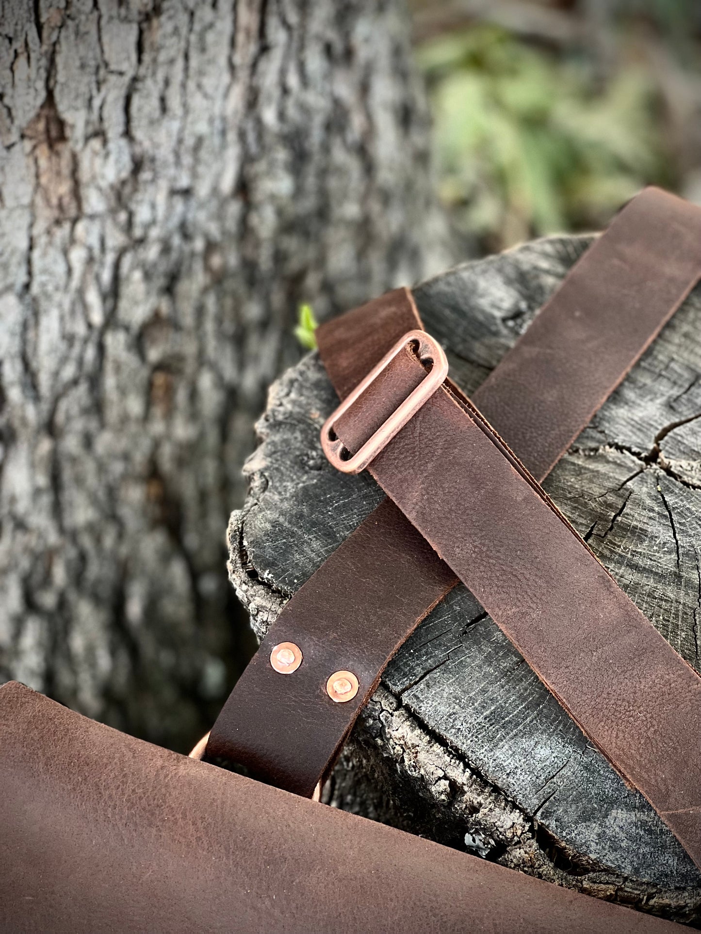 Detail of The Culper Haversack's leather strap and copper hardware on a rustic wooden surface.