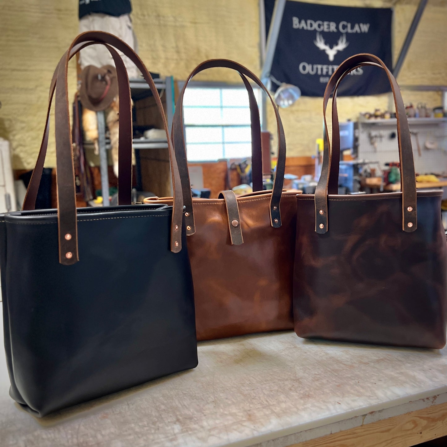 Three Hill Country Tote bags in black, tan, and brown leather with classic design and sturdy straps.