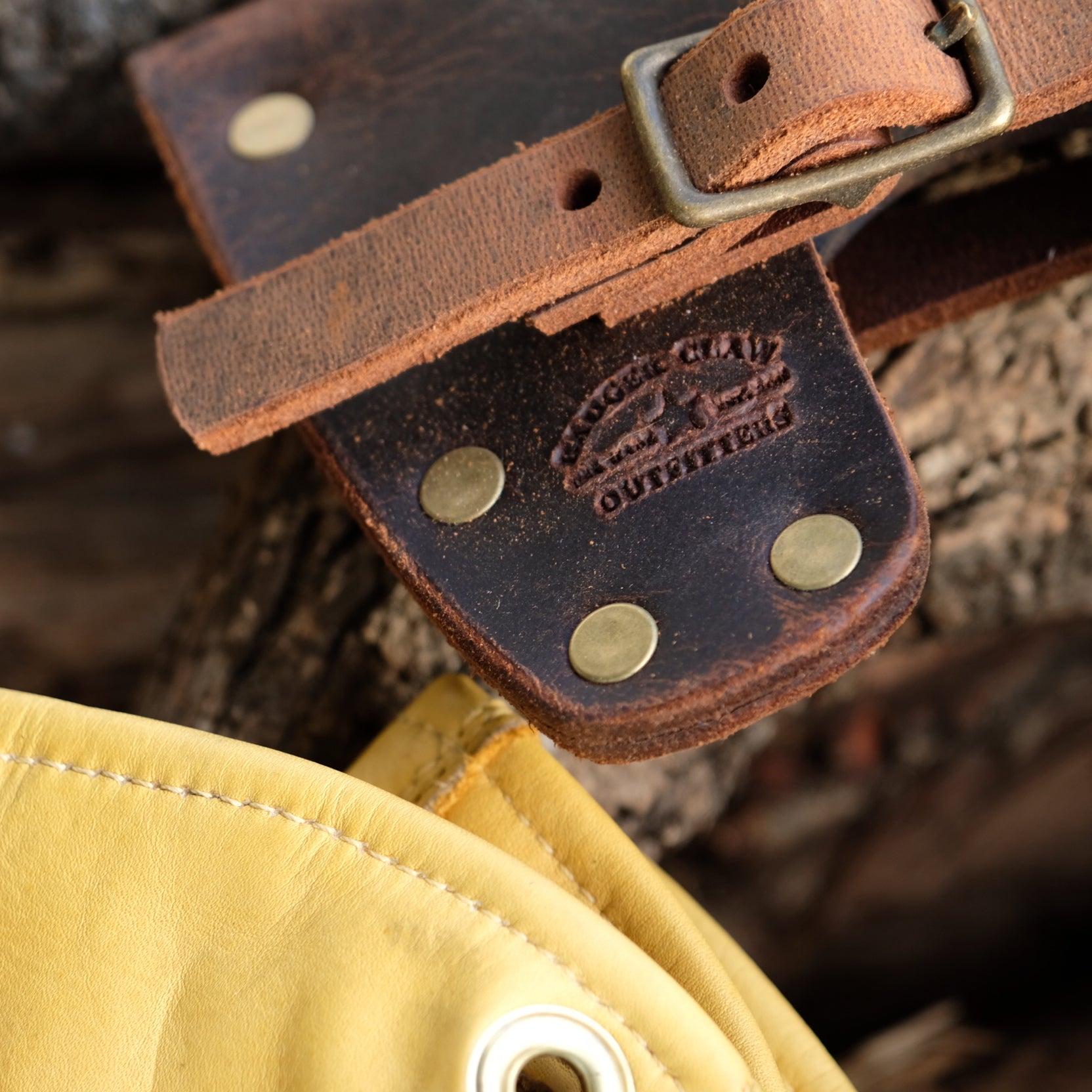Close-up of a premium Crazy Horse leather axe mask strap with brass studs and logo on wood background.
