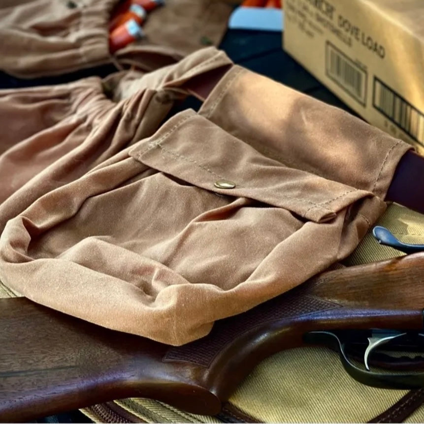 Close-up of a russet brown shotgun shell pouch on a table, showcasing its antique brass snap and elastic opening.