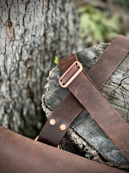 Detail of The Culper Haversack's leather strap and copper hardware on a rustic wooden surface.