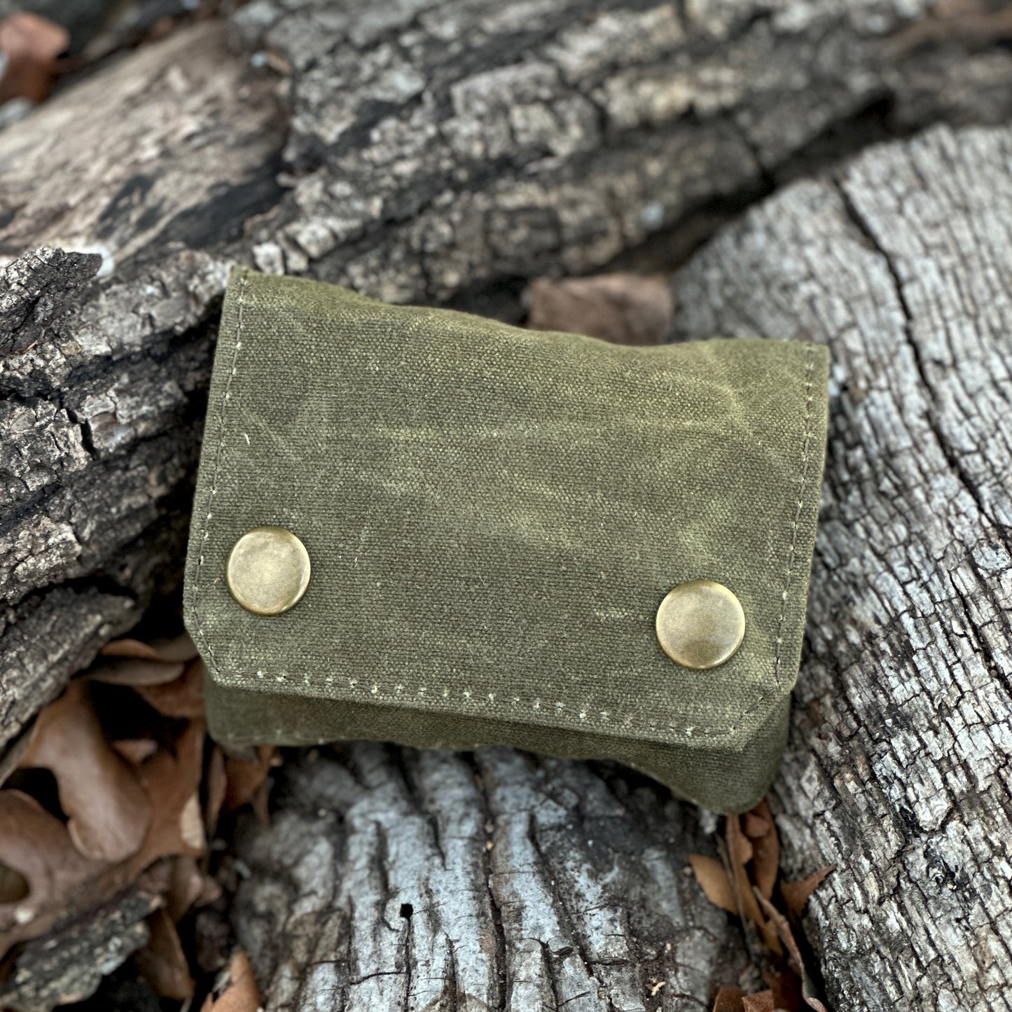 Small seasoning kit in waxed canvas design, featuring snap closures, resting on natural wood background.