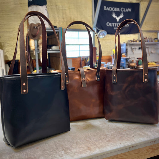 Three Hill Country Tote bags in black, tan, and brown leather with classic design and sturdy straps.