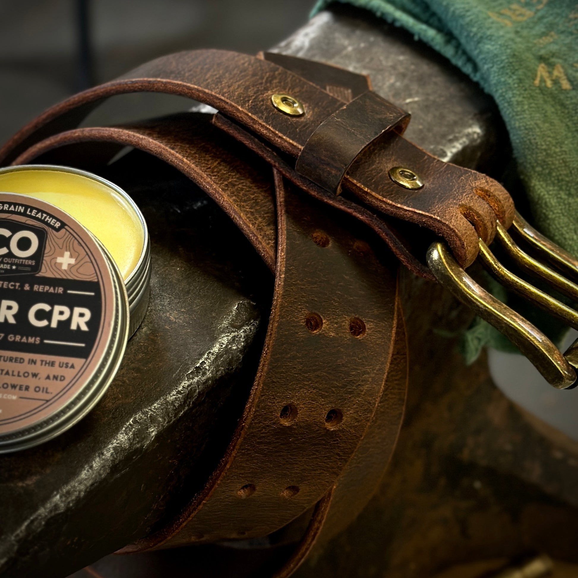 Close-up of a rustic Ranch Belt made from Crazy Horse leather, next to leather conditioner on a workbench.